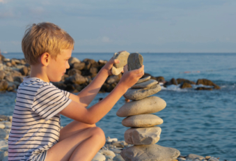 enfant qui construit un cairn de galets sur la plage.