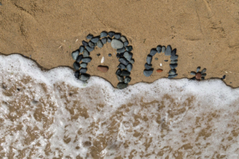 dessin de visage en galets sur la plage, léchés par les vagues