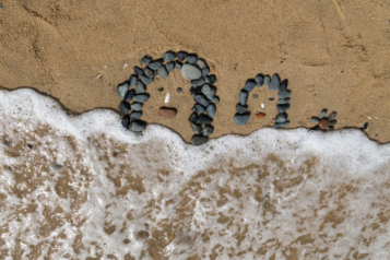 dessin de visage en galets sur la plage, léchés par les vagues