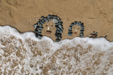 dessin de visage en galets sur la plage, léchés par les vagues