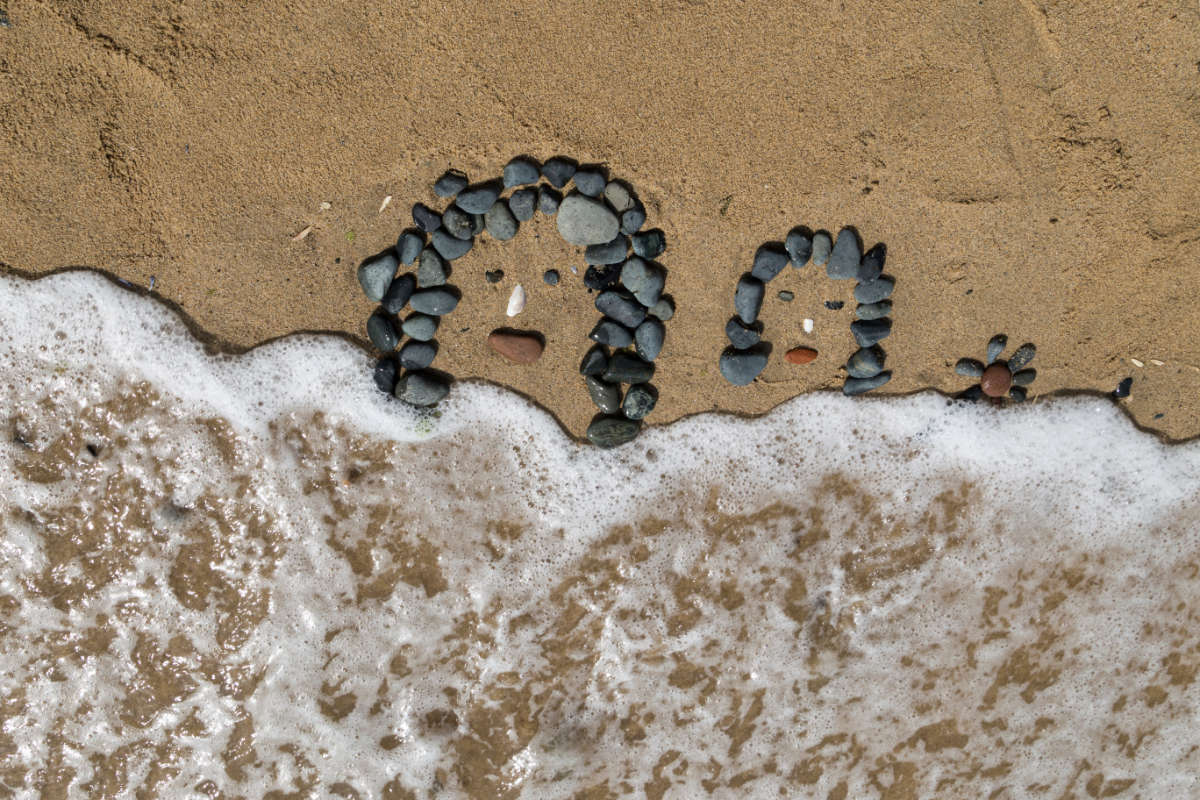 Dessin de visage en galets sur le sable au bord de l'eau.