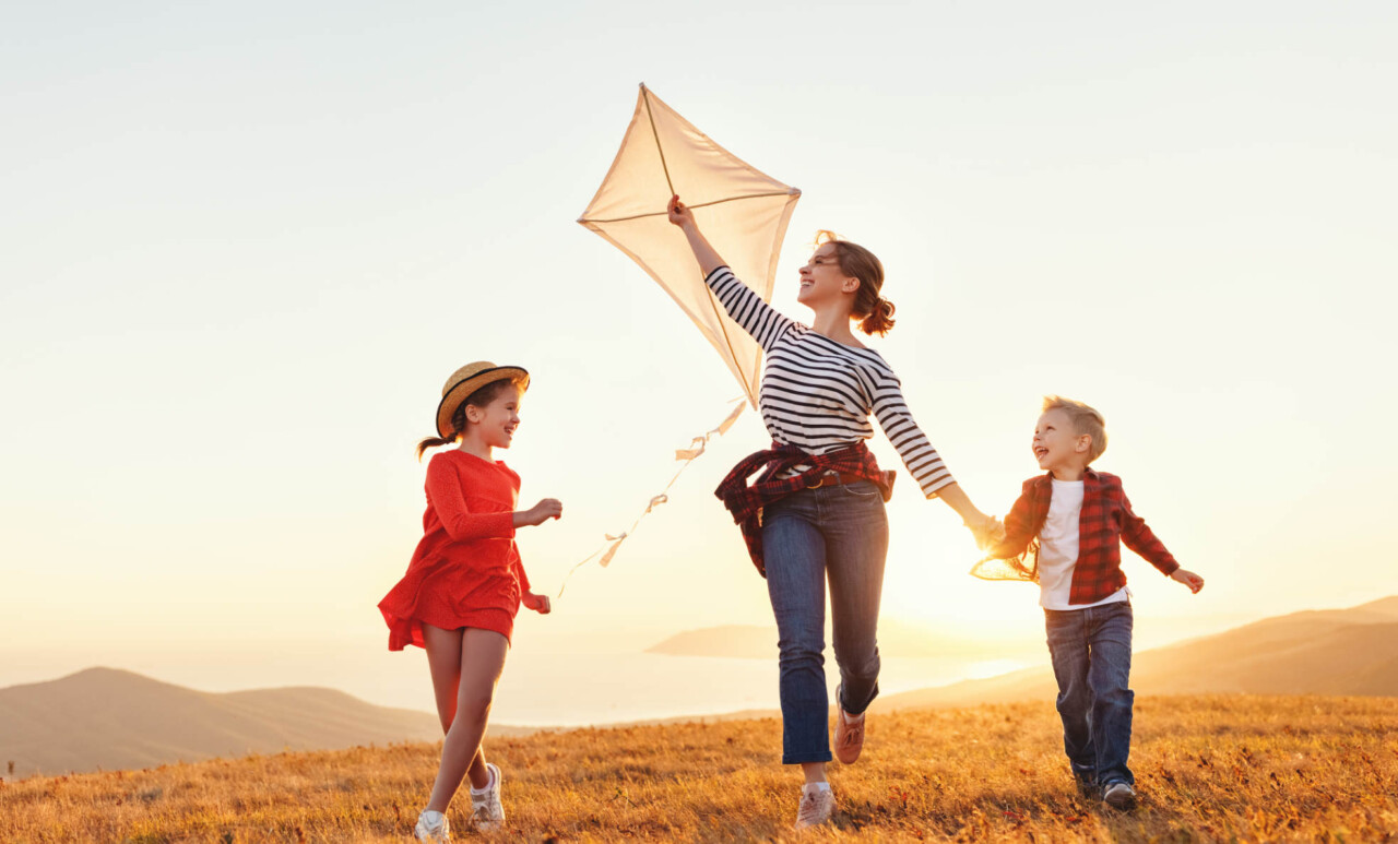 Une femme et deux enfants courent pour faire voler un cerf-volant.