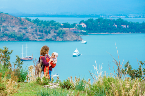 Maman et son bébé en porte-bébé devant un paysage maritime.