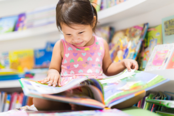 Petite fille lit un livre en bibliothèque.