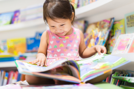 Petite fille lit un livre en bibliothèque.